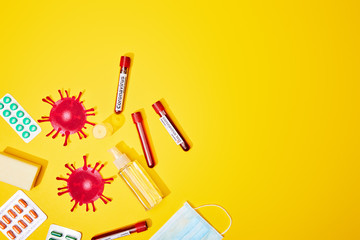 top view of test tubes with coronavirus test lettering near medical mask, blister packs with pills, bottle with antibacterial liquid and soap bar on yellow