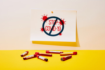 paper with stop covid-19 lettering near test tubes with blood samples on white and yellow
