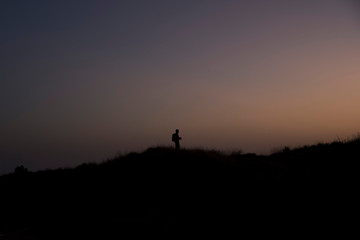 Fototapeta na wymiar Men standing on hill photographing at sunset