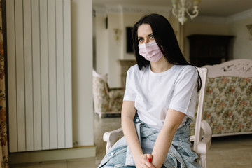 Sad lonely girl isolated at home in protective sterile medical mask on her face looking at window, bored woman because of Chinese pandemic coronavirus, virus covid-19. Quarantine, prevent infection