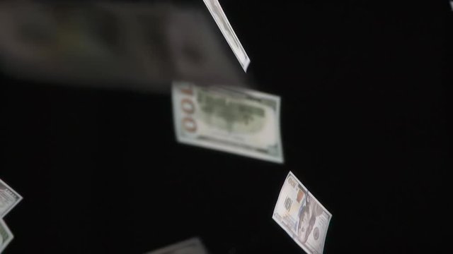 Cash Flow. Loop. Monetary denominations of $ 100 in a large number of slowly falling down on black background. Filmed at a speed of 240fps