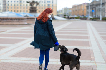 Young female using a face mask as a coronavirus spreading prevention walking with her dog. Global...