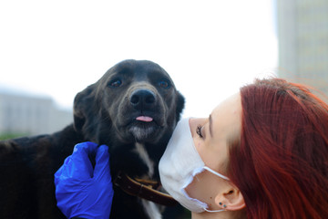 Young female using a face mask as a coronavirus spreading prevention walking with her dog. Global...