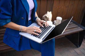 Stylish business lady on lunch break while working out of office. Freelancer working with pc in summer city. Fahionable female manager sit on the bench in the city park and typing.