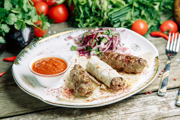  Restaurant dish on a wooden background with vegetables. Lula kebab in lavash with pomegranate and onion on a plate.