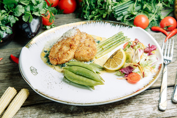 Restaurant dish on a wooden background with vegetables. Chicken cutlet with asparagus and peas on a plate.