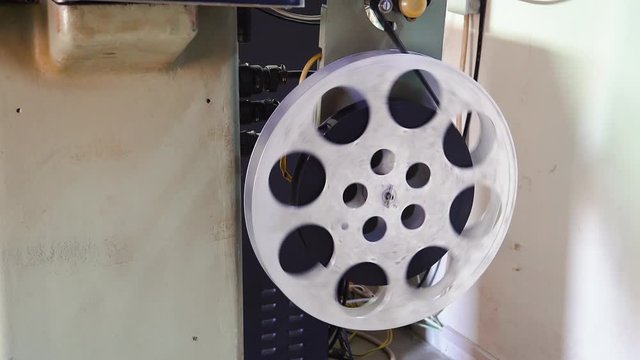 CU: old film reel coiled on large spool of retro cinema projector equipment to show historic movie in projection booth closeup