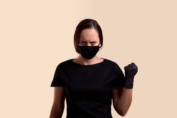 woman in black dress face mask and gloves threatens with a fist and looking at camera