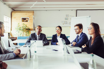 Group of smiling analysts communicating during meeting. Cheerful young business people talking during briefing. Business meeting concept