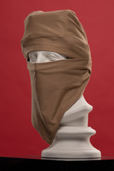 White plaster statue of a bust of Apollo Belvedere in hijab niqab