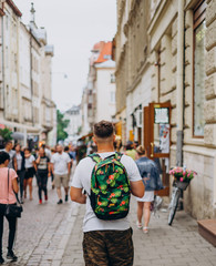 A man with a backpack on a city tour in the summer. A young man walks the city on a sunny day. Sports guy in shorts and with a colored backpack.
