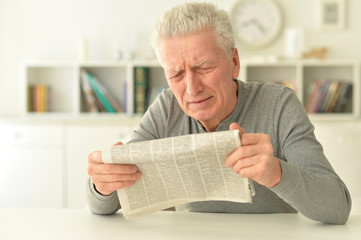 Emotional senior man reading newspaper at home