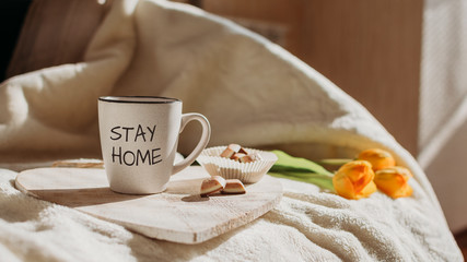 Fototapeta na wymiar Stay home, Stay safe, Save Lives, quarantine, Help Stop Coronavirus concept. Anti-stress survival routine During Coronavirus Crisis. Cup with text Stay home and sweets on the bed in morning sun