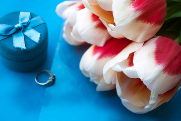 Bouquet of tulips and a box with a wedding ring on a blue background. Concept of marriage proposal.