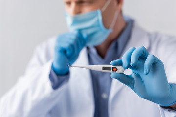 selective focus of mature doctor in latex gloves holding digital thermometer and coughing isolated on grey