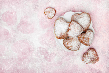 Homemade heart shaped donuts with powdered sugar on pink background. Tasty doughnuts on cute pink pastel background