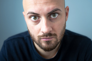 closeup guy with beard and green eyes looking directly into the camera. beautiful eyes and a beautiful look. blurred blue background