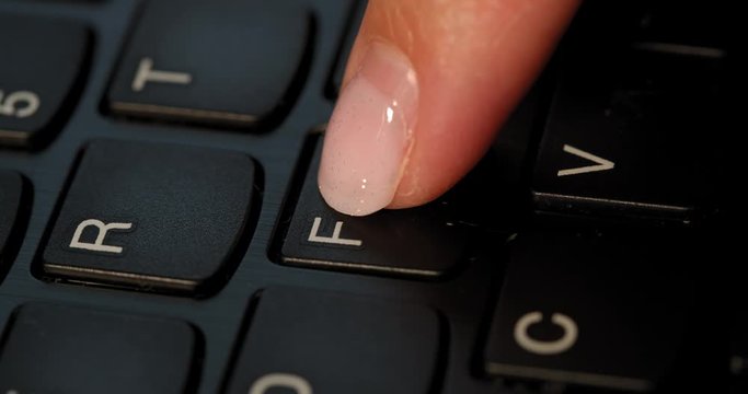 Black keyboard and a girl pushes F button. English letters. Slow-mo and girl has a pink nail polish.