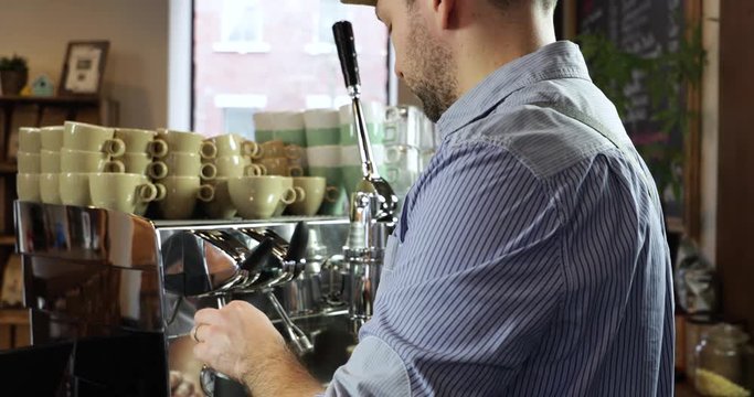 Vintage barista man preparing foaming milk in a black pitcher on an authentic Italian coffee machine.