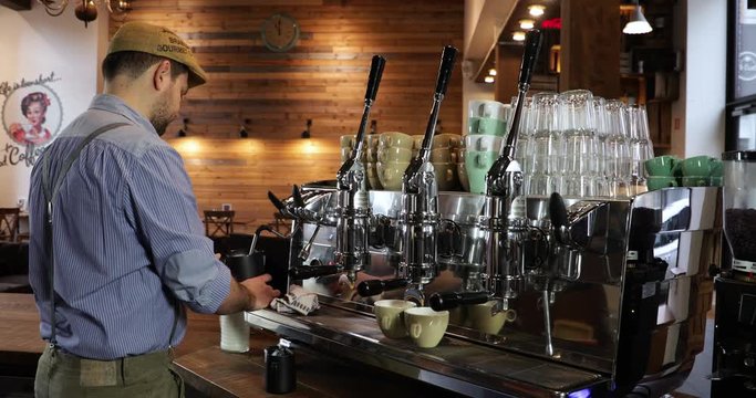 Vintage barista at work. Process of making coffee. Man with a beard. Preparing cappuccino on an Italian coffee machine at a vintage coffee shop. Foaming milk in a pitcher and pouring milk in a cup.