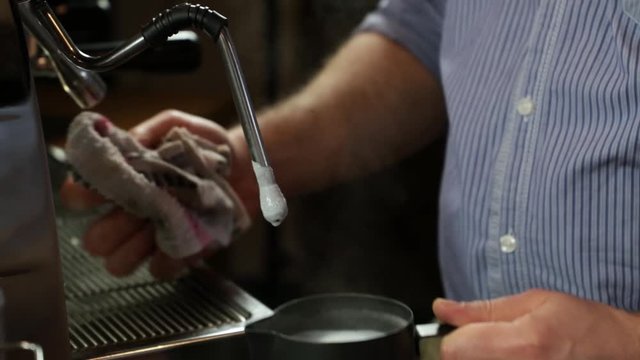 Close-up of a vintage barista man preparing foaming milk in a black pitcher to prepare a cappuccino.