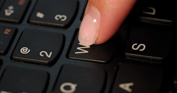 Black keyboard and a girl pushes W button. English letters. Slow-mo and girl has a pink nail polish.