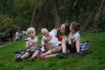 Naklejka na ściany i meble Three children and mom enjoying a picnic in summer. Togetherness concept with kids. Friendly family siblings
