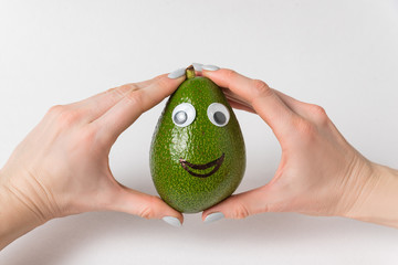 Female hands holds avocado with funny face. Avocado with Googly eyes and smile.
