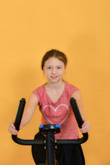 The girl goes in for sports, the child on a stationary bike does cardio and looks forward to the camera.