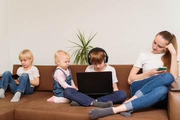 Four children of different ages sitting on couch with phones and laptop. Dependence on social networks.