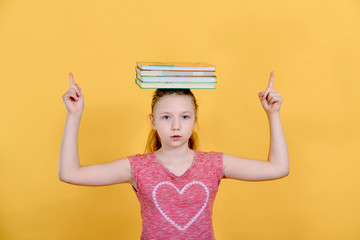 Girl holds books on her head and raises her hands to the top, student child on a yellow background.