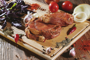 Pickled raw meat lies on a light board with tomatoes cherry, red pepper, basil, garlic and seasoning.