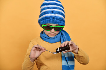 A boy in a blue hat and scarf pours medicine and bottles for the treatment of colds, flu and...