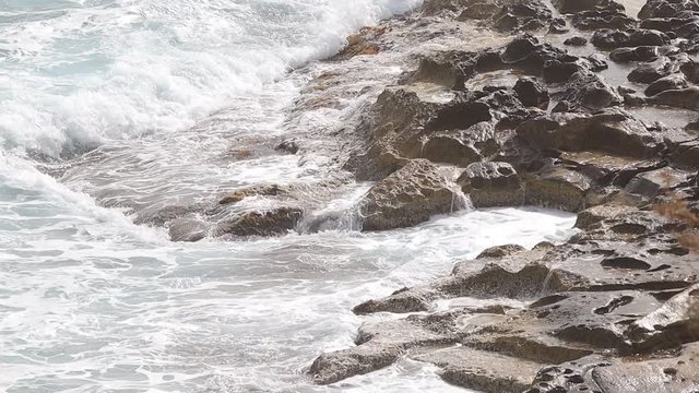 Sea waves are splashing against the hard rocks at the beach of Sliema. Close up of waves splashing against rocks. Sea nature film.