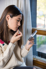 A teenager applying a lipstick with a mirror in her hand
