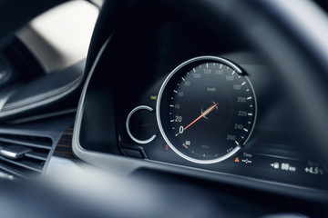 Close-up of the speedometer on the dashboard of a modern expensive car. The dashboard illumination is reflected. Front background is blurred