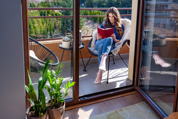 Beautiful young reading a book on the balcony