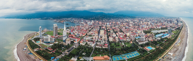 Aerial panoramic image of beautiful Batumi made by drone in cloudy weather. Capital of Adjara in Georgia, located on coast of Black Sea. Old and new city. Mountains on the background. Skyscrapers.