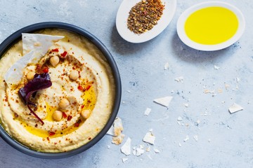 Classic hummus in a bowl with herbs, smoked paprika, olive oil and lettuce on a blue (gray) background. Healthy vegan food. A dish of Middle Eastern cuisine. Healthy eating concept.