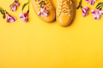 Pair of yellow sneakers and flower buds on yellow background. Spring summer fashion concept