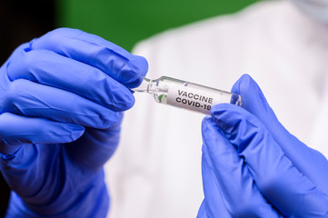 A medical worker in a protective suit holds an ampoule with a coronavirus vaccine
