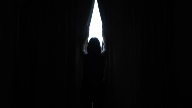 young slim woman silhouette opens large window heavy curtains in sunny morning in hotel room backside view
