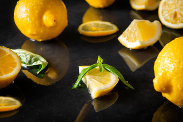 lemons with Basil on a wet black surface, yellow citrus