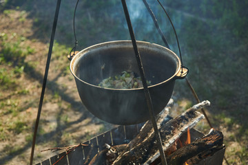 Food is prepared in a cauldron. The bowler boils at the stake, in the background is a flower...