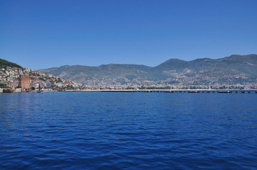 Fototapeta na wymiar A magnificent view of the calm blue sea, the city on the mountain and the sky. Beautiful summer day on the sea shore.