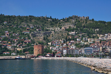 The tower of the medieval fortress stands on the sea. The fortress protects the city located on the mountain.