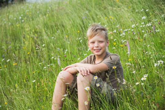 Portrait of handsome happy smiling caucasian kid sitting in fresh green grass in countryside meadow.