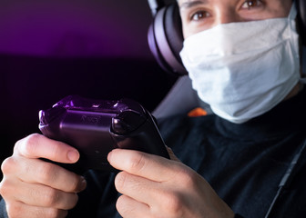 Young white man playing video games with medical mask on his face while Covid-19 quarantine