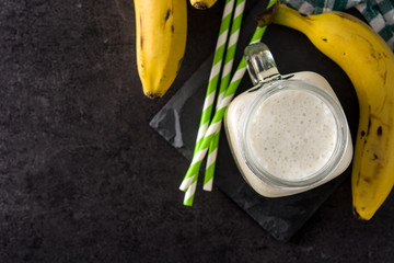 Banana smoothie in jar on black slate background. Top view. Copy space