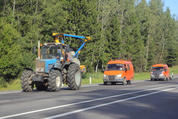 Tractor and orange special mini bus on roadside on trees background ay Sunny summer day, forest maintenance service in Russia